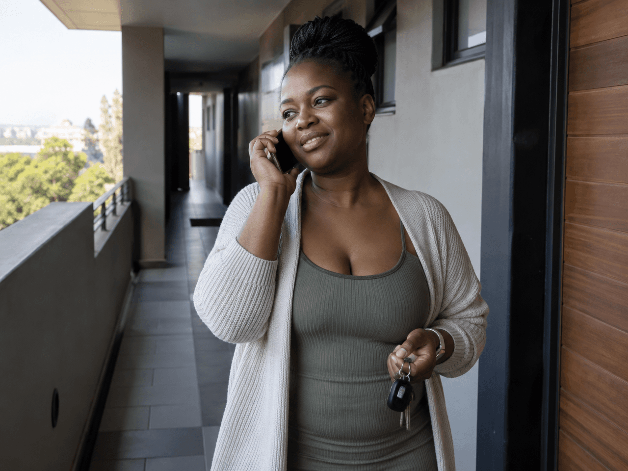 A woman on a phone call in an apartment corridor, holding keys